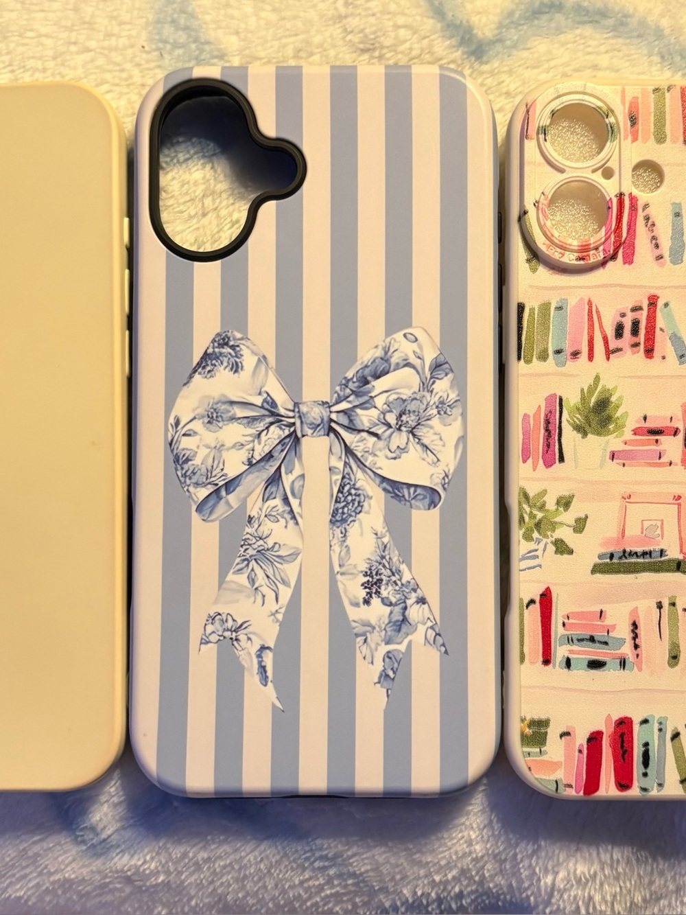 Three I Phone 16 Plus cases:  blue stripe with bow, bookshelves, & cream